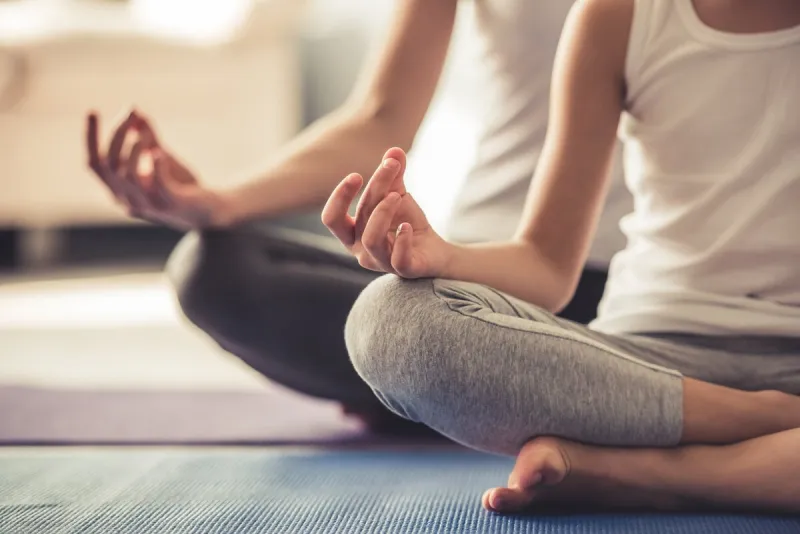 cropped image of young woman and her little daughter doing yoga together at home