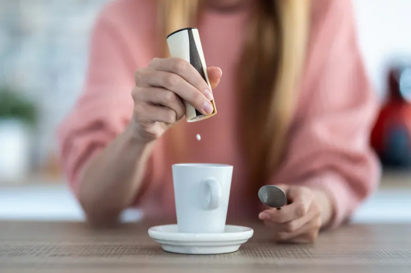 close-up of woman hand throwing saccharin pills on coffee cup in the kitchen at home
