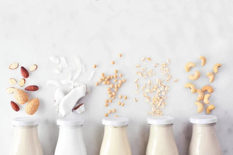 vegan, plant based, non dairy milk variety in milk bottles with ingredients above view over a white marble background
