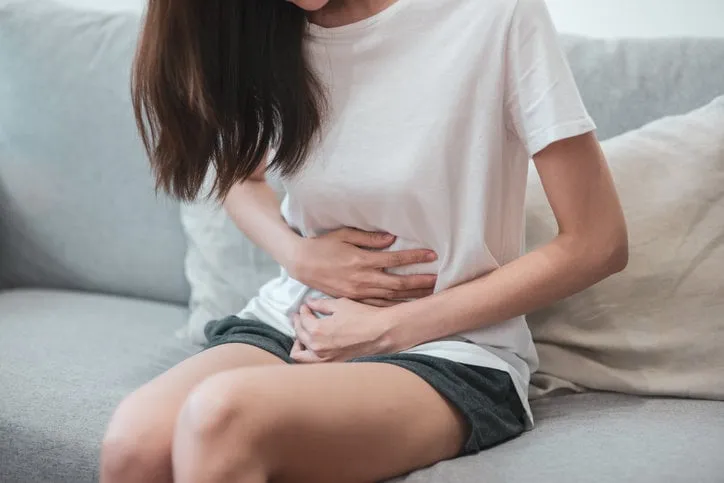 healthcare medical or daily life concept   close up stomach of young lady have a stomachache or menstruation pain sitting on a sofa