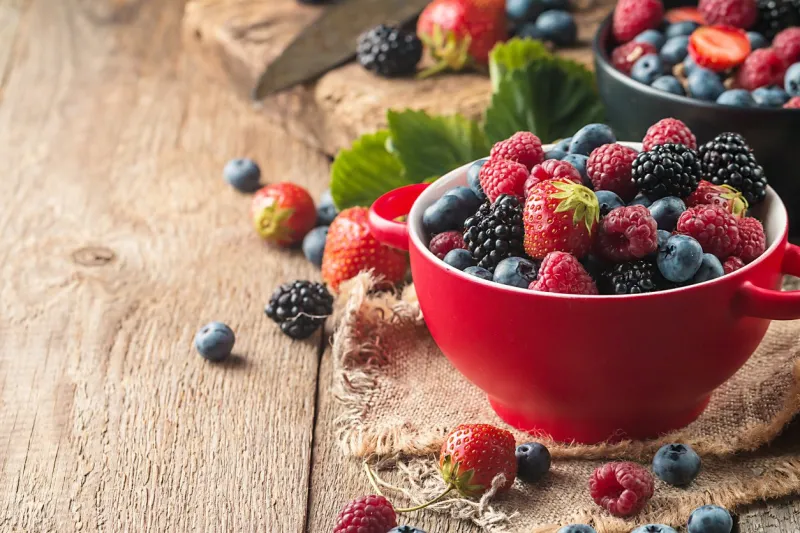 ripe sweet different berries in red bowl on rustic wooden table harvest concept