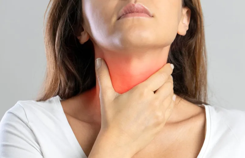 sore throat, woman with pain in neck, gray background, studio shot