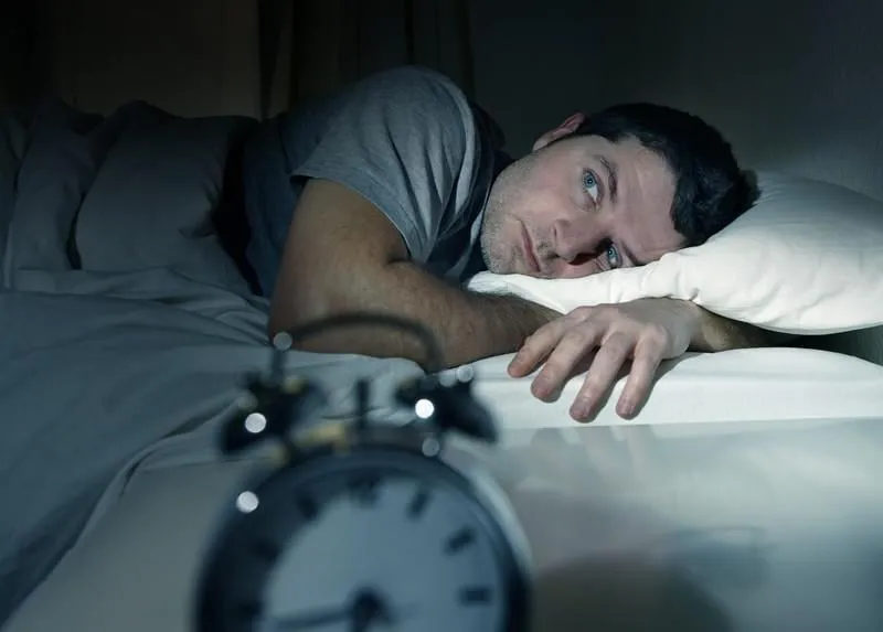 jeune homme au lit avec les yeux ouverts souffrant d'insomnie et de troubles du sommeil en pensant à son problème