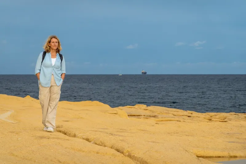 valletta, malta a tourist woman walks along a rocky shore next to the mediterranean sea