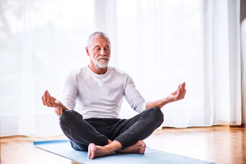active senior man meditating at home, eyes closed