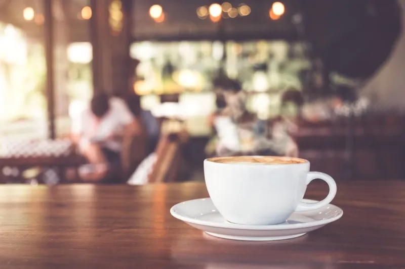 cup of hot coffee on table in cafe with people vintage and retro color effect - shallow depth of field