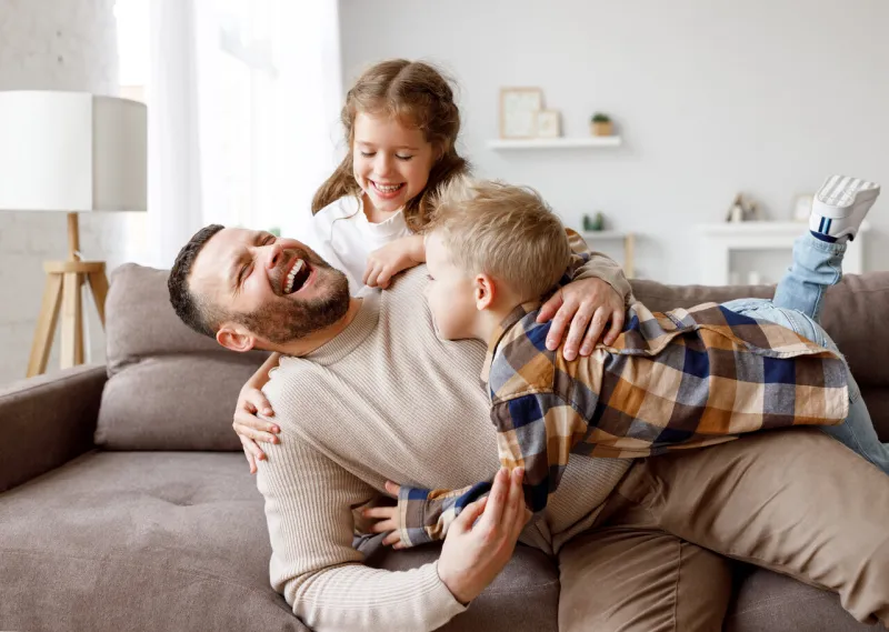 happy girl and boy playing with bearded man on couch on weekend day at home