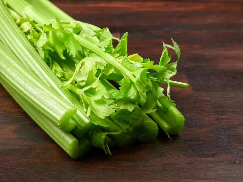 fresh green celery stalks on a dark rustic wooden oak board