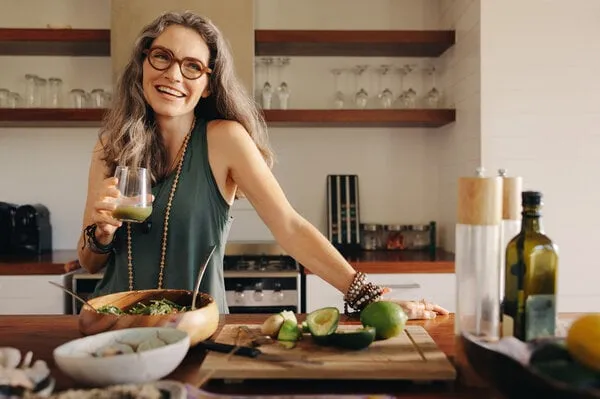 healthy senior woman smiling while holding some green juice in her kitchen mature woman serving herself wholesome vegan food at home happy woman taking care of her aging body with a plant-based diet