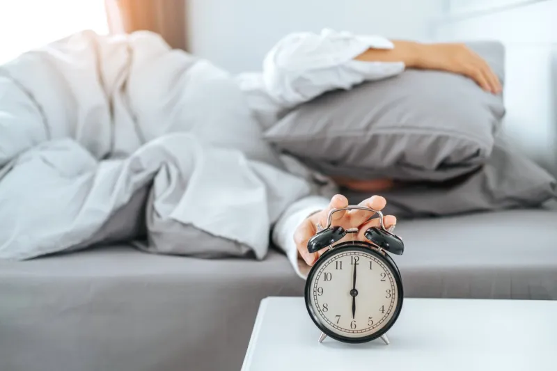 close up clock on the bed asian woman wake up and disturbed by alarm clock early morning
