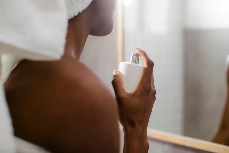 unrecognisable woman standing at bathroom and spraying perfume on her neck