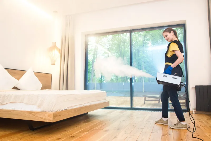 professional cleaning service woman in uniform and gloves does the cleaning in a cottage treatment, disinfection of the apartment with hot steam from odors and parasites, bed bugs
