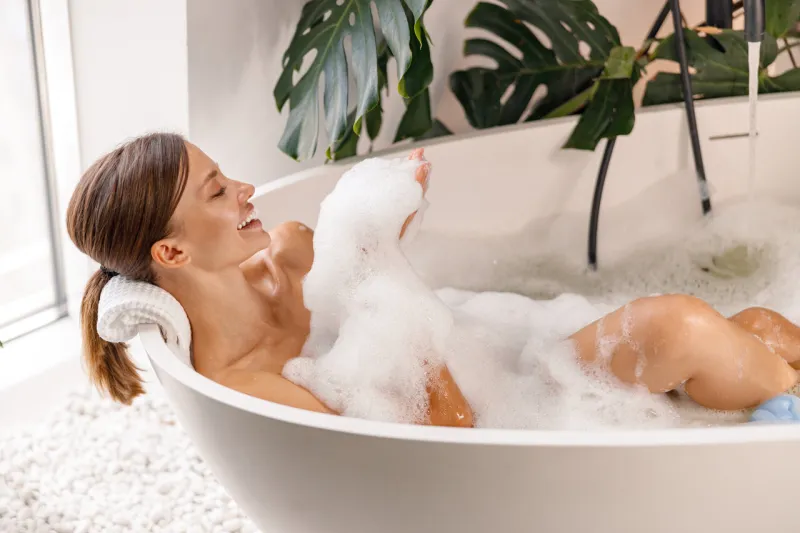 bathing young woman relaxing in bath, smiling and playing with bubble foam body care, wellness concept