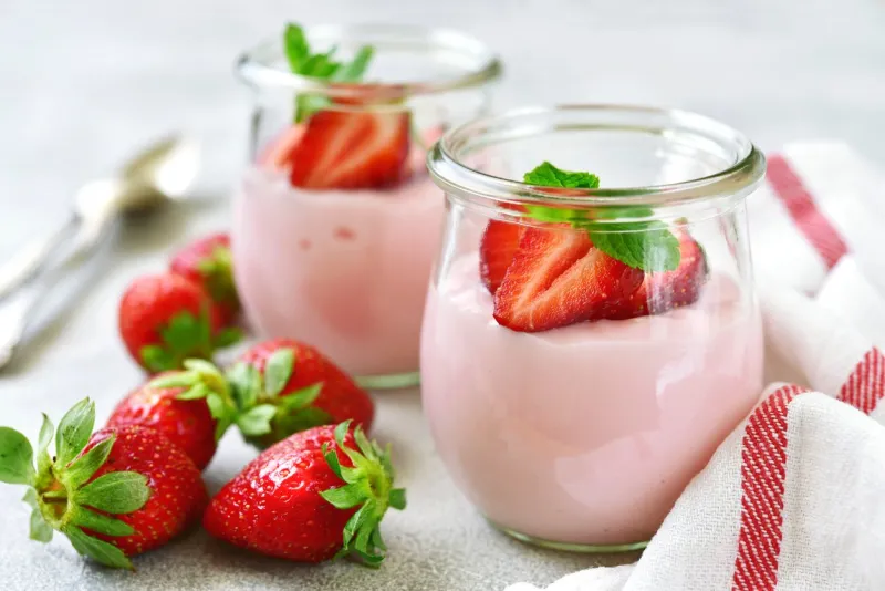 natural strawberry yogurt with fresh berry and mint in a vintage glass jar on a light slate, stone or concrete background