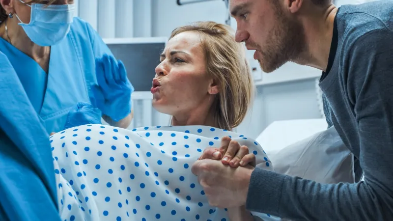 in the hospital, close-up on a woman in labor pushing hard to give birth, obstetricians assisting, spouse holds her hand modern maternity hospital with professional midwives