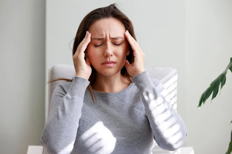 shot of a young woman holding her head in discomfort due to pain at home