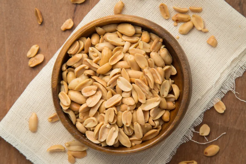 roasted peanuts in wooden bowl putting on linen and wooden background