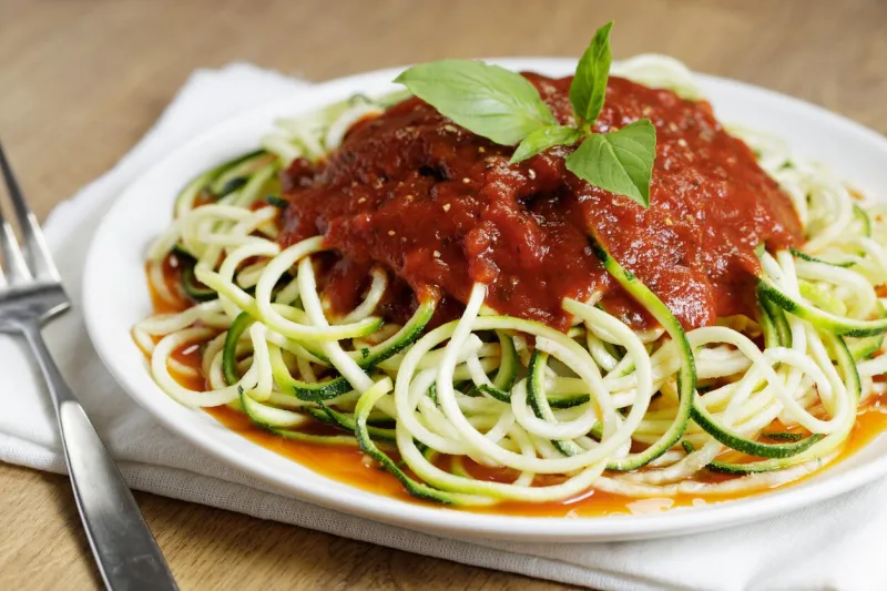 zucchini pasta with tomato sauce in white plate on wooden table