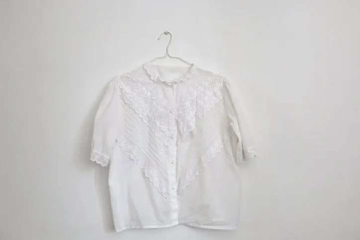 vintage white lace blouse hanging on a white wall