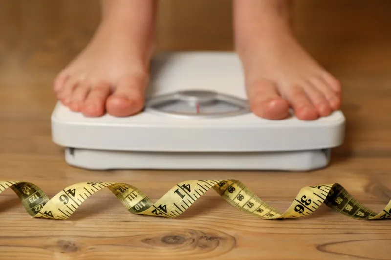 overweight girl using scales near measuring tape on wooden floor, selective focus