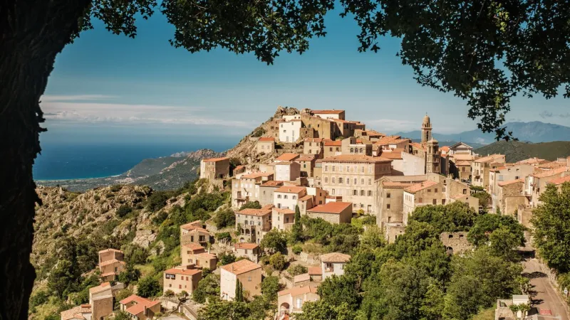 the iconic perched mountain village of speloncato in the balagne region of corsica on a bright sunny day framed by a tree
