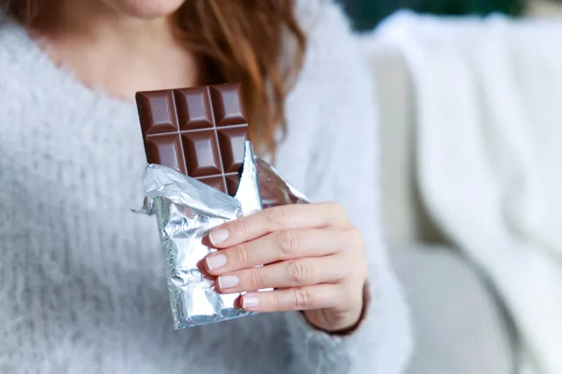hands of a woman holding a tile of chocolate chocolate bar in silver foil in woman's hand