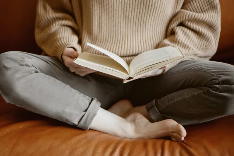cropped image of woman sitting on the couch and reading a book close up