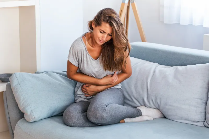 woman lying on sofa looking sick in the living room beautiful young woman lying on bed and holding hands on her stomach woman having painful stomachache on bed, menstrual period