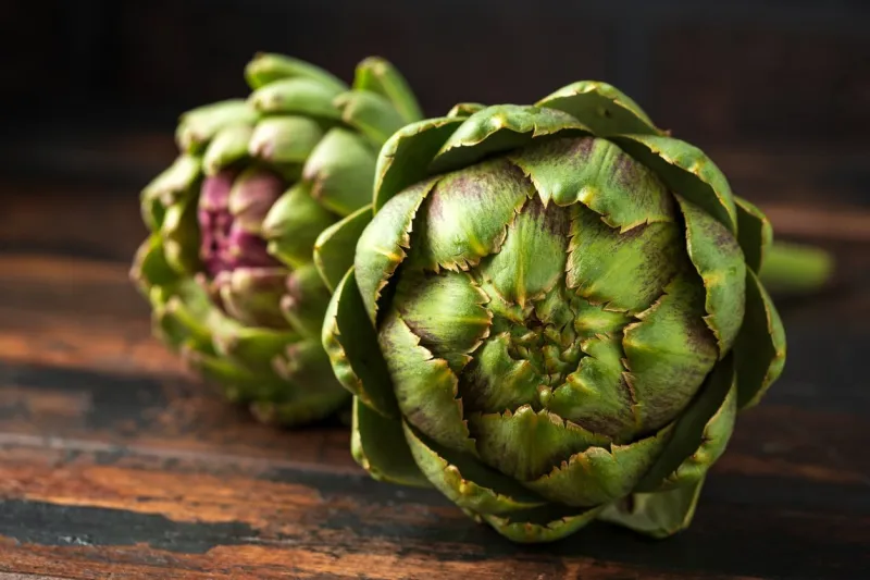 fresh raw organically grown artichoke flower buds on wooden table