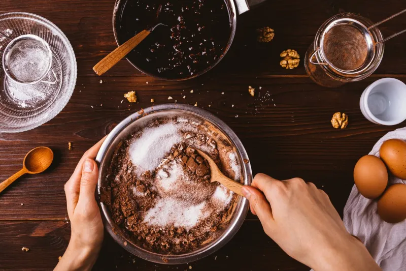 top view female hands mix cocoa powder, sugar and flour to make dough with melted chocolate and walnuts for delicious homemade brownie cake