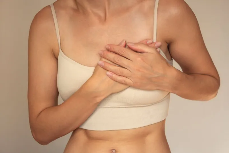 a young woman in beige underwear holds the left side of her chest with both hands from pain, suffers from arrhythmia, difficulty breathing, panic attacks women's health
