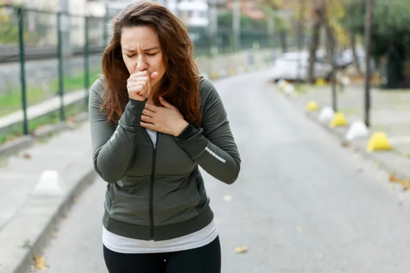 young sporty woman coughing while walking on the street athlete woman affected by air pollution during running training