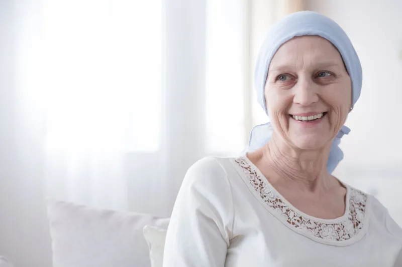 upper body portrait of an older, female cancer patient looking happy and hopeful in a bright white interior