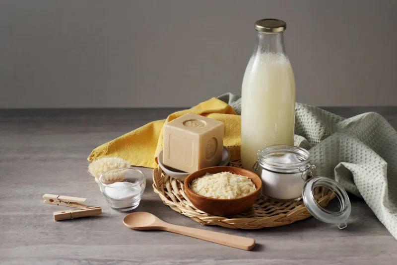 traditional hard soap bar from marseille (france), pure soap flakes, baking soda, cotton towel, spoon, clothes peg and home made washing up liquid in the glass bottle on the grey table