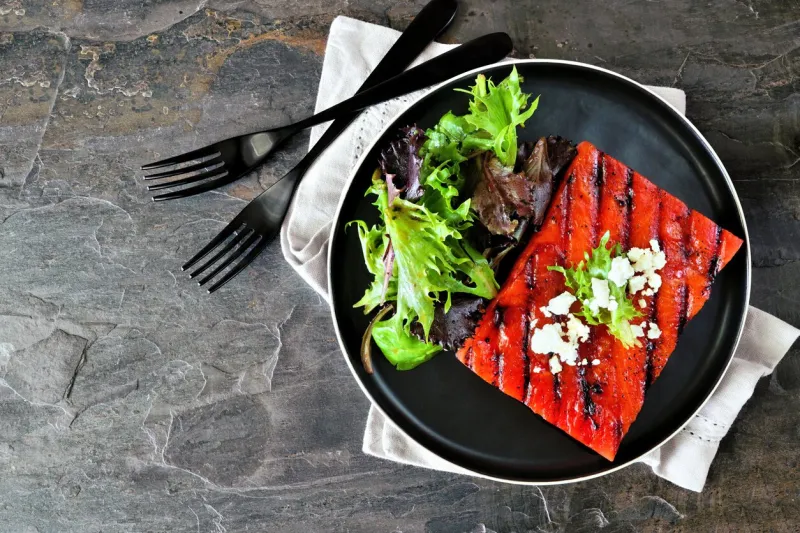 grilled watermelon steak with salad top view table scene on a dark slate background healthy eating, plant based meat substitute concept
