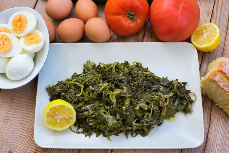 salad with boiled wild greens, dandelion, lemons and extra virgin olive oil, on a wooden table