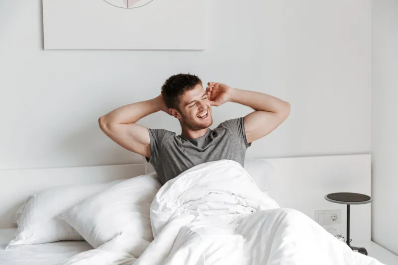 attractive young man stretching hands in bed at home