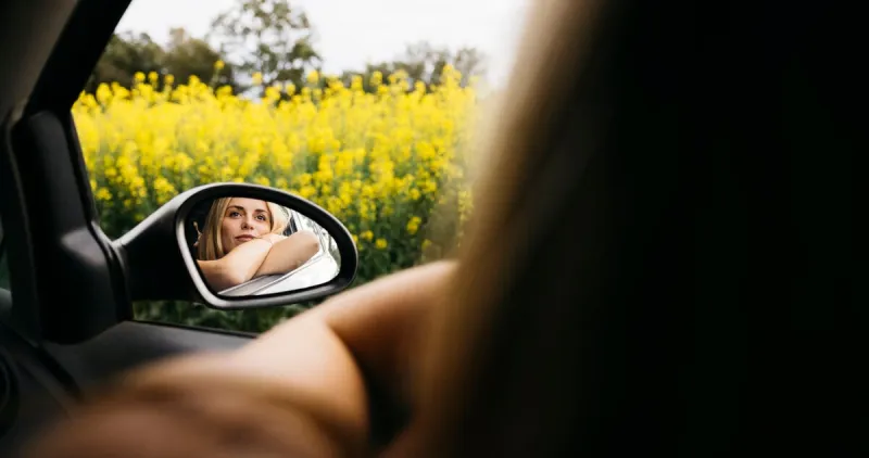 young smiling woman sitting in car and leaning on window during her road trip and enjoying beautiful spring day in nature