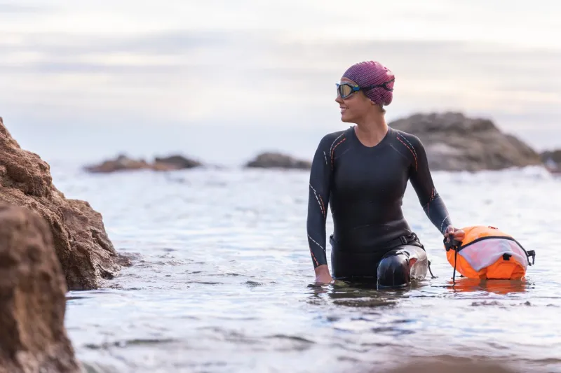 portrait of a woman swimming in open water with wetsuit and buoy