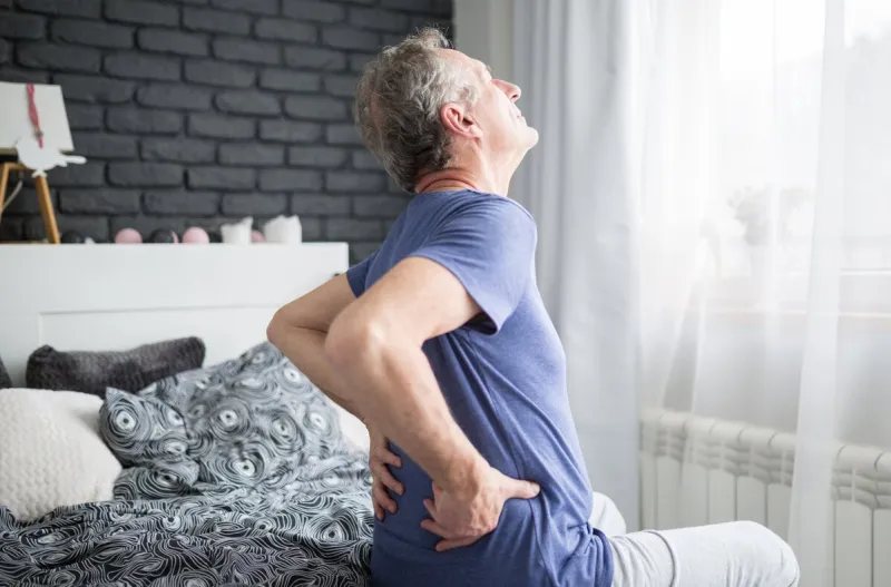 portrait of senior man with lower back pain siting on bed
