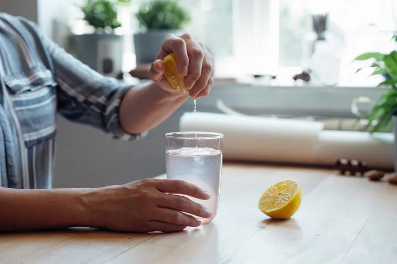 close up shot of an anonymous young woman's hands squeezing a lemon into a cup of water making lemonade sitting at a wooden table