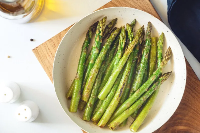 top view on roasted asparagus in a white pan on a kitchen table modern style, vegetarian food