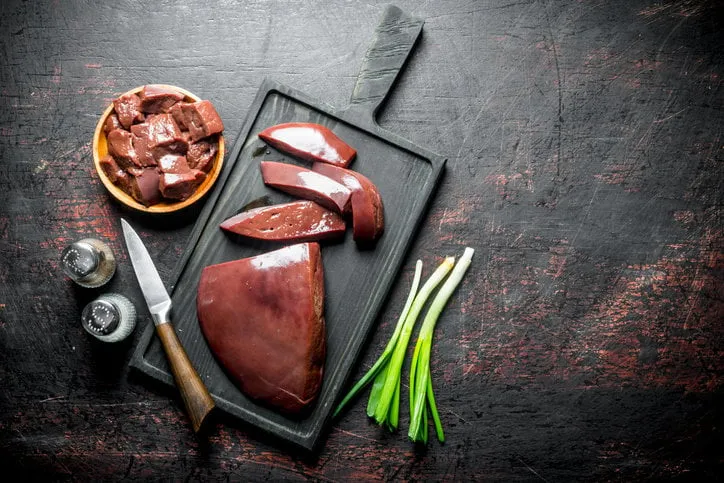 pieces of raw liver in a plate and on a cutting board on dark rustic background