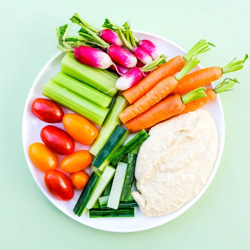 fresh vegetable crudite platter with hummus and baby carrots, radishes, cucumber, celery and tomatoes