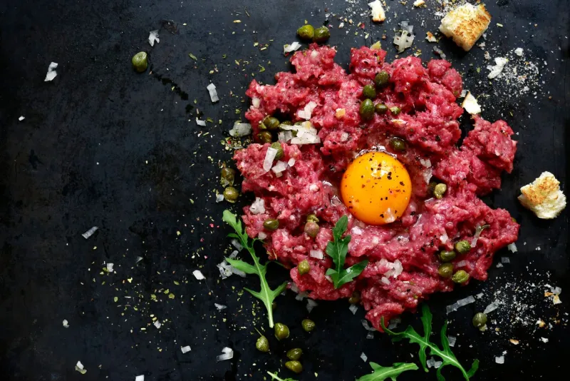 beef tartare on a black slate or metal background- traditional dish of french cuisinetop view