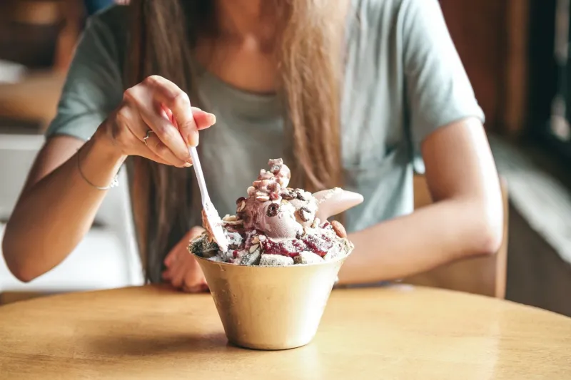 female young lady eat korean bingsu ice with chocolate icecream with ricecake and nuts selective focus on bingsu blur people