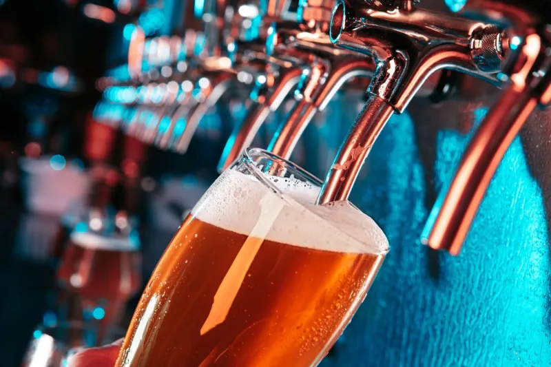hand of bartender pouring a large lager beer in tap bright and modern neon light, males hands pouring beer for client side view of young bartender pouring beer while standing at the bar counter
