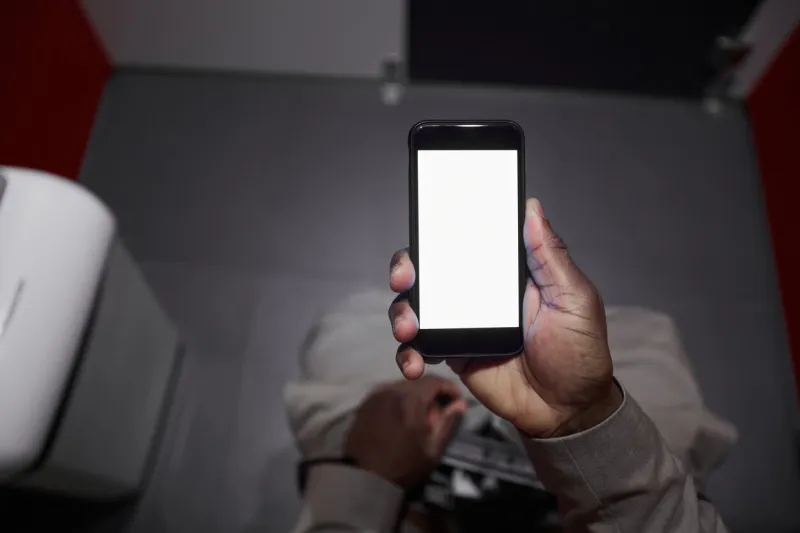 top view closeup of unrecognizable african-american man using smartphone while sitting on toilet in public restroom, copy space
