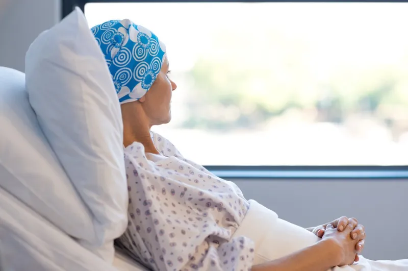 young woman in bed suffering from cancer thoughtful woman battling with tumor looking out of window young patient with blue headscarf recovery in hospital on bed