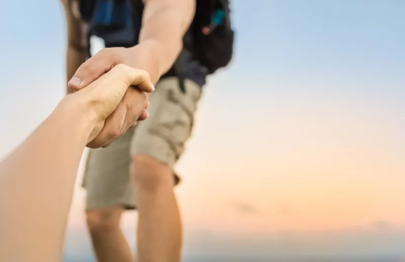 hiker giving his hand helping partner climb up to the top of mountain